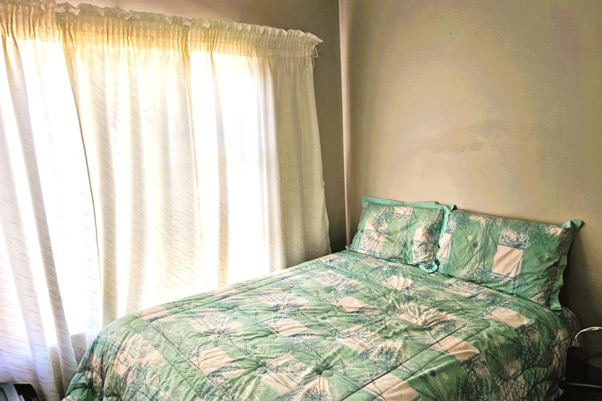 A bedroom featuring a window with curtains and visible wall staining, requiring cosmetic attention to improve the overall presentation.