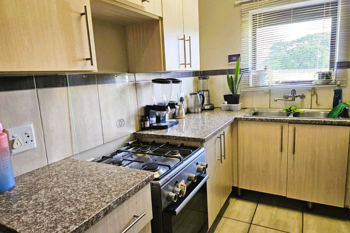 A functional kitchen featuring light wood-finish cabinetry, granite countertops, a gas stove with oven, and a tiled backsplash with a window view.