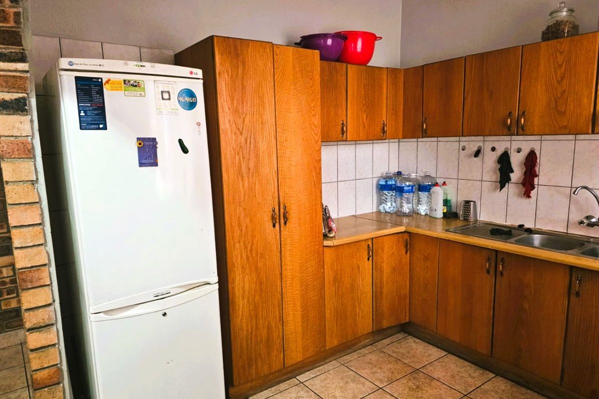 A functional kitchen featuring wood-look laminate cabinetry, tiled backsplash, and ceramic flooring, offering a practical layout with ample storage space.
