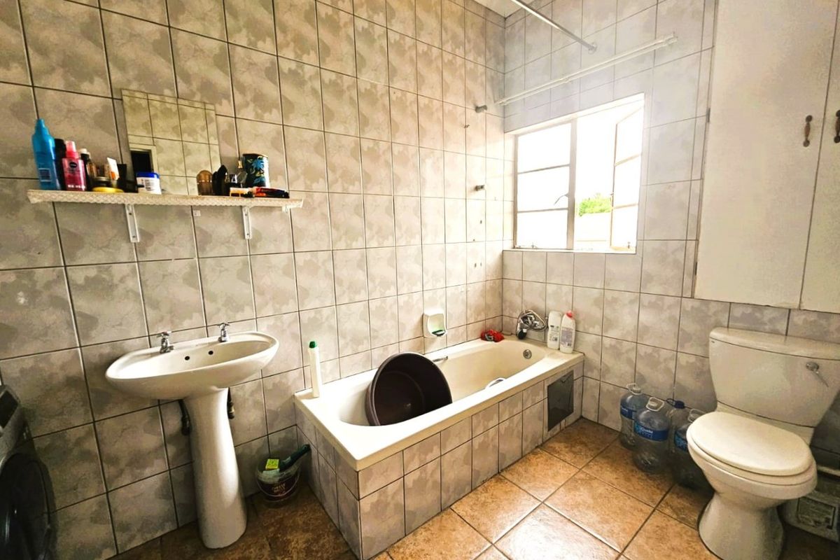 A dated bathroom featuring a pedestal basin, tiled bathtub, and toilet, with full-height wall tiling and a window for natural light.