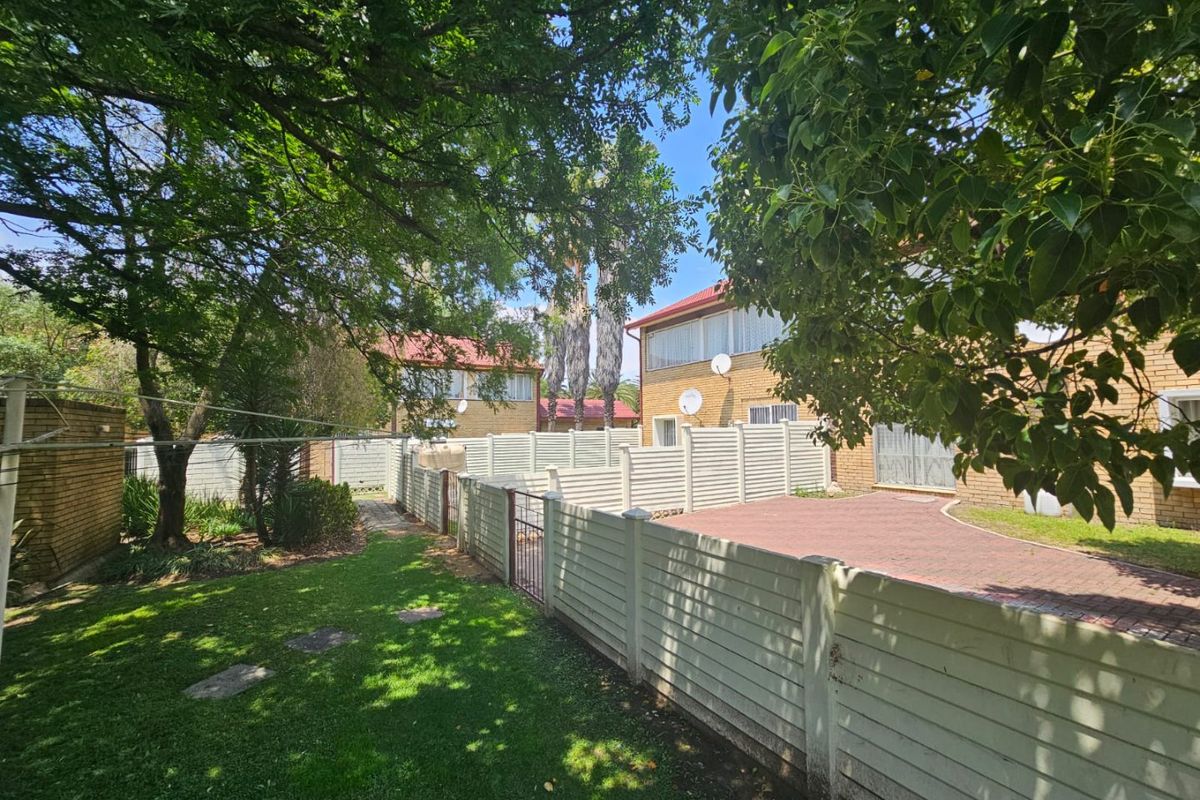 A rear view of the property featuring a paved driveway, a secure precast concrete boundary wall, and a well-maintained garden area.