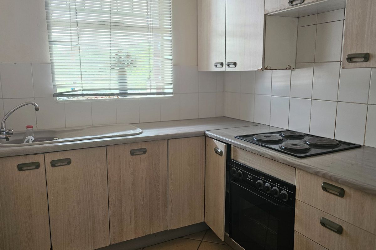 A functional kitchen featuring laminate cabinetry, a built-in oven with electric hob, tiled backsplash, and a stainless steel sink under a window.