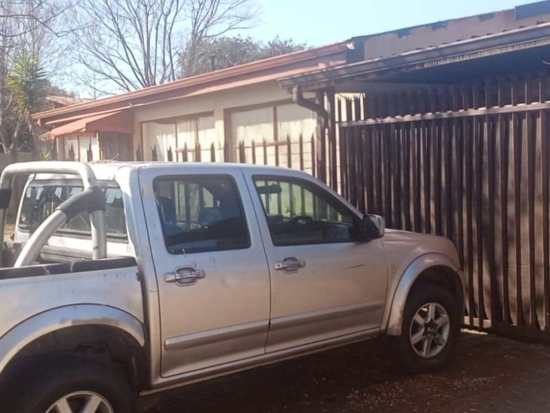 Front exterior view of the property featuring a security gate and perimeter fencing, showing signs of weathering and maintenance requirements.
