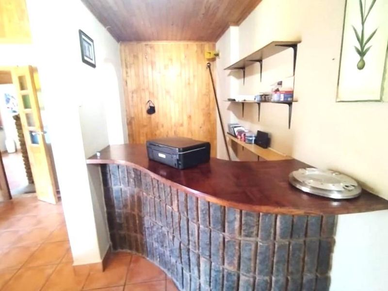A rustic bar area featuring a stone-clad counter, timber wall paneling, wood-paneled ceiling, and built-in wall shelving.