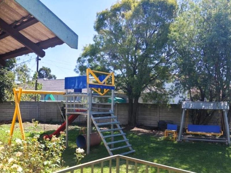 A private backyard garden featuring a lawn, mature trees, and a precast concrete boundary wall.