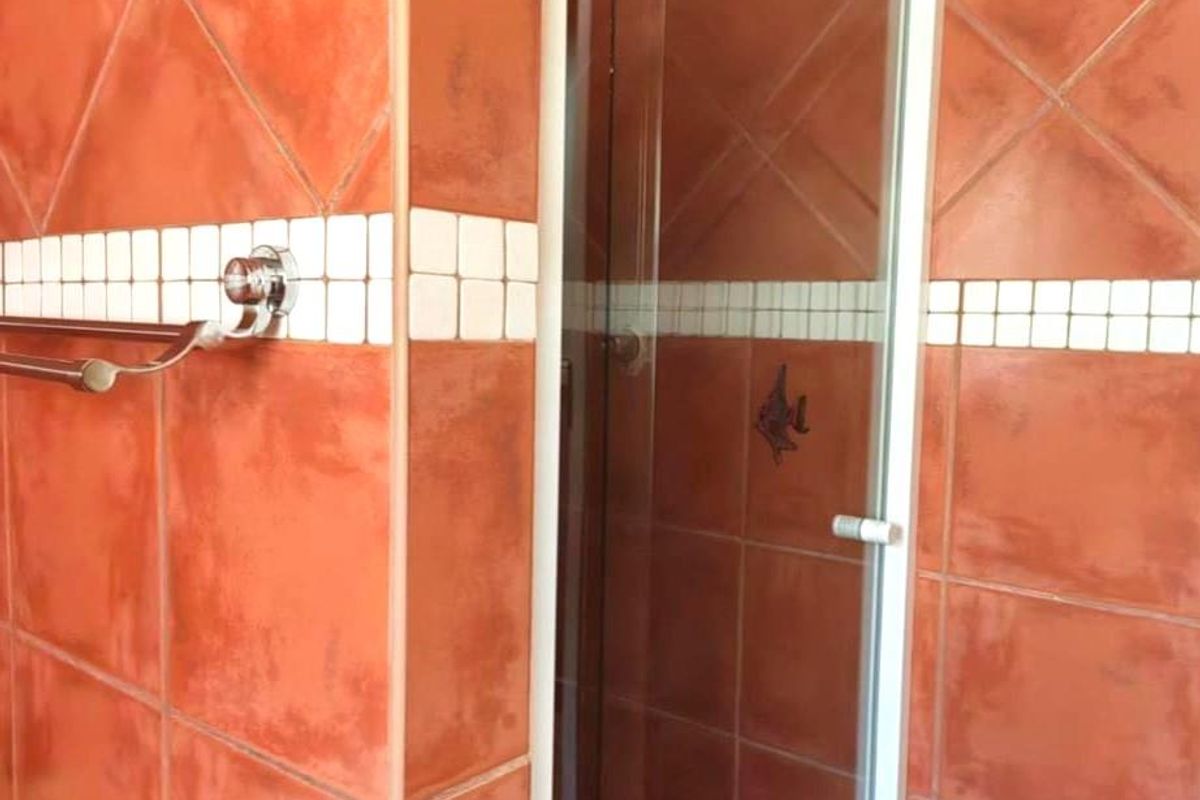 A bathroom featuring terracotta-toned wall tiles with a decorative border and a built-in shower enclosure.