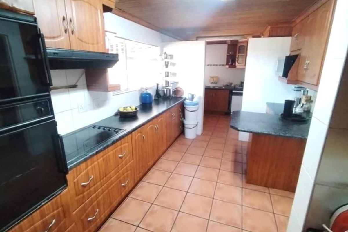 A functional kitchen featuring extensive wooden cabinetry, integrated oven, electric hob, and tiled flooring, offering a traditional layout with ample storage space.