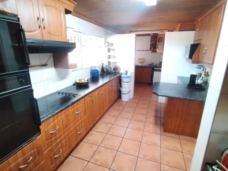 A functional kitchen featuring extensive wooden cabinetry, integrated oven, electric hob, and tiled flooring, offering a traditional layout with ample storage space.
