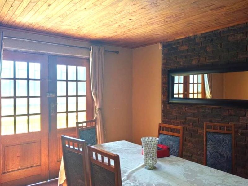 Dining room featuring a rustic exposed brick wall, timber ceiling, and classic french doors providing natural light.