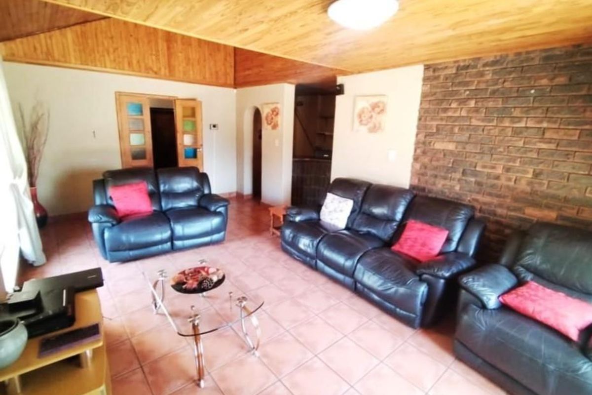 Spacious living room featuring a rustic exposed brick wall, warm timber ceiling, and tiled flooring, offering a comfortable and character-filled lounge area.