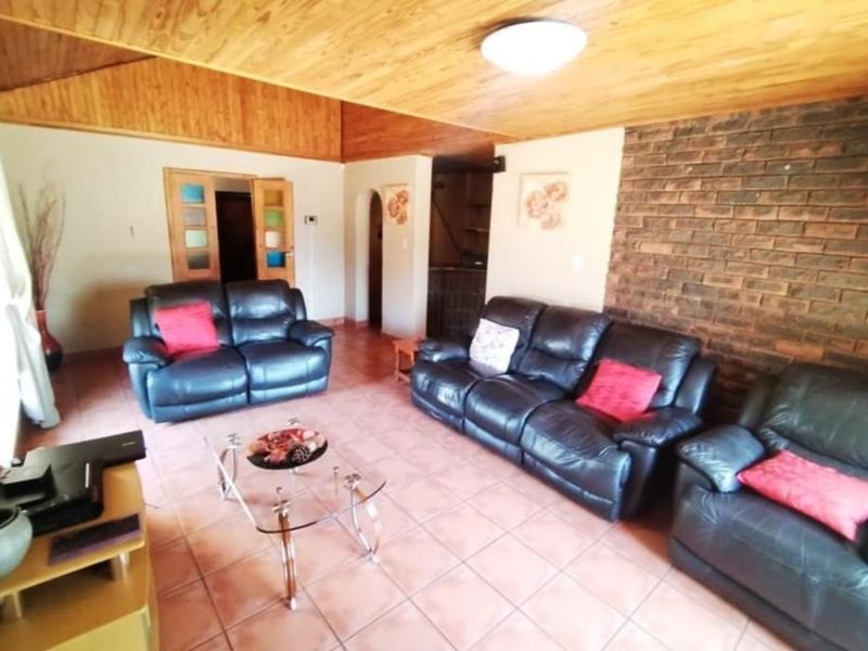 Spacious living room featuring a rustic exposed brick wall, warm timber ceiling, and tiled flooring, offering a comfortable and character-filled lounge area.