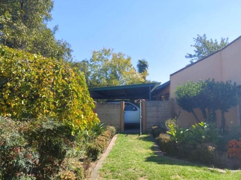 Front view of the property featuring a landscaped garden, paved walkway, and a covered carport area.