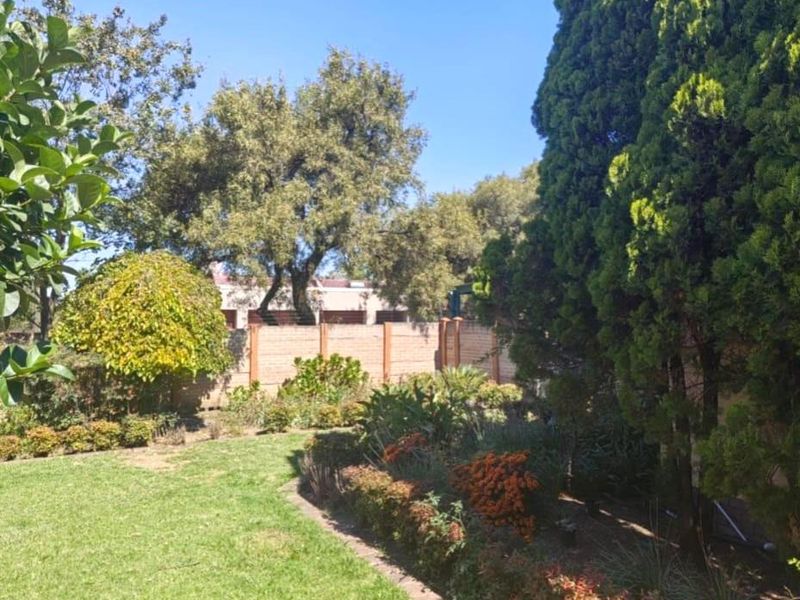 A well-maintained private garden featuring established trees, landscaped garden beds, a neat lawn, and a secure brick boundary wall.