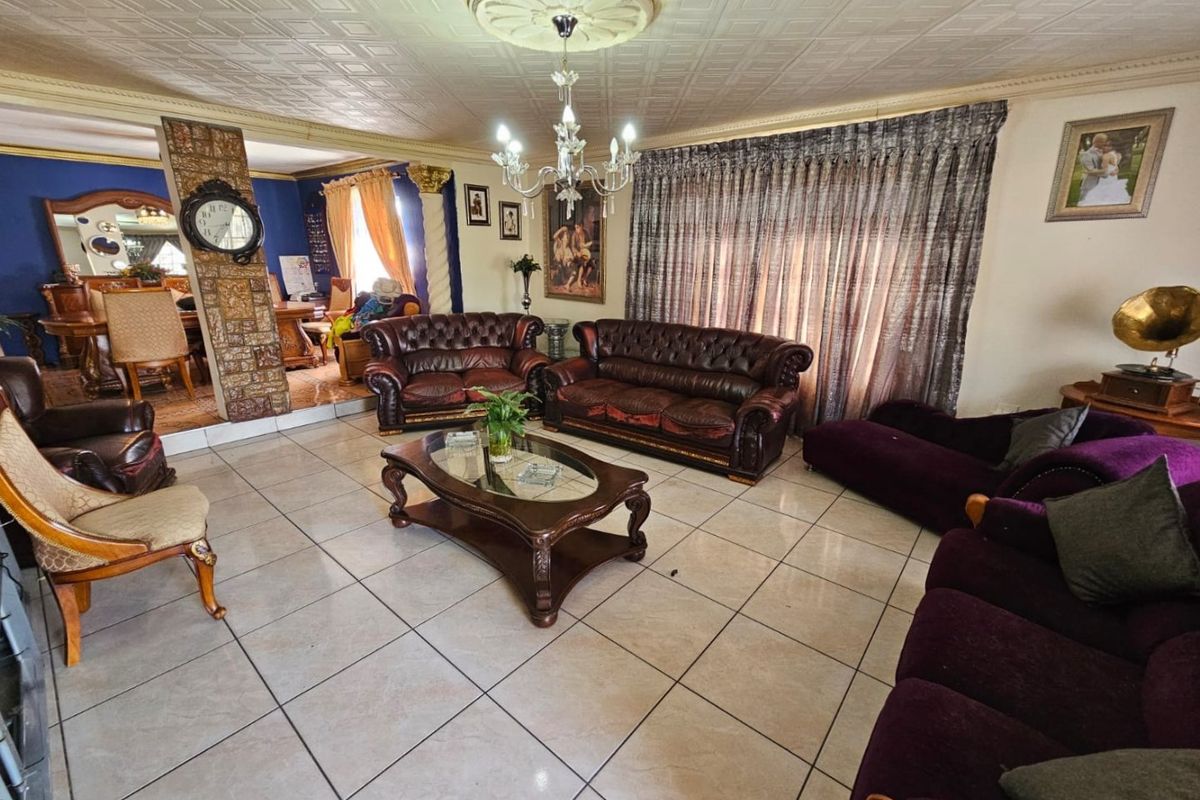 Spacious living area featuring tiled flooring, a decorative ceiling rose with chandelier, and a unique stone-clad pillar accent.