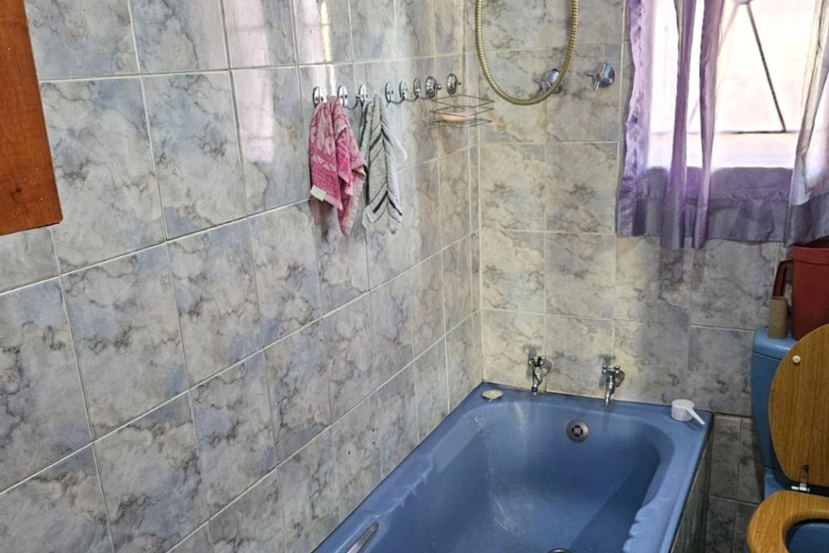 A dated bathroom featuring blue sanitary ware, tiled walls, and a shower-over-bath configuration, offering potential for a modern renovation.