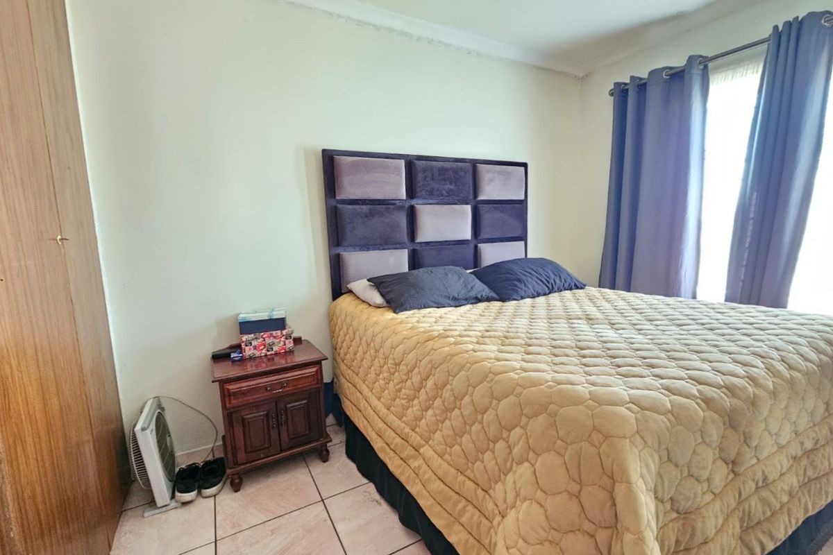 A bedroom featuring tiled flooring and a built-in wardrobe, showing signs of wear on the ceiling and cornice.