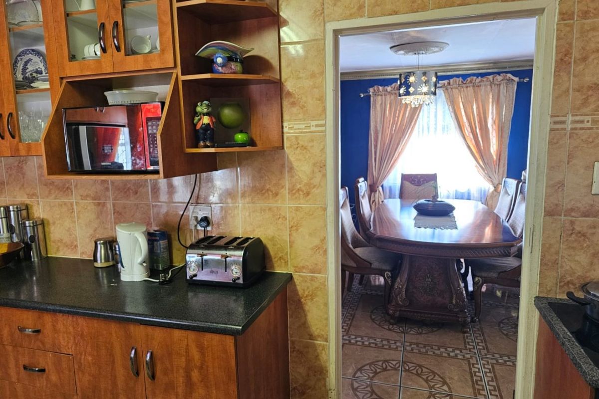 A functional kitchen featuring wood-finish cabinetry and tiled walls, with a direct view into the adjacent dining area.