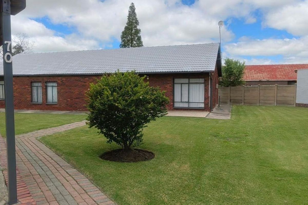 A well-maintained rear exterior view featuring a brick facade, tiled roof, paved walkway, and a spacious lawn area with timber fencing.