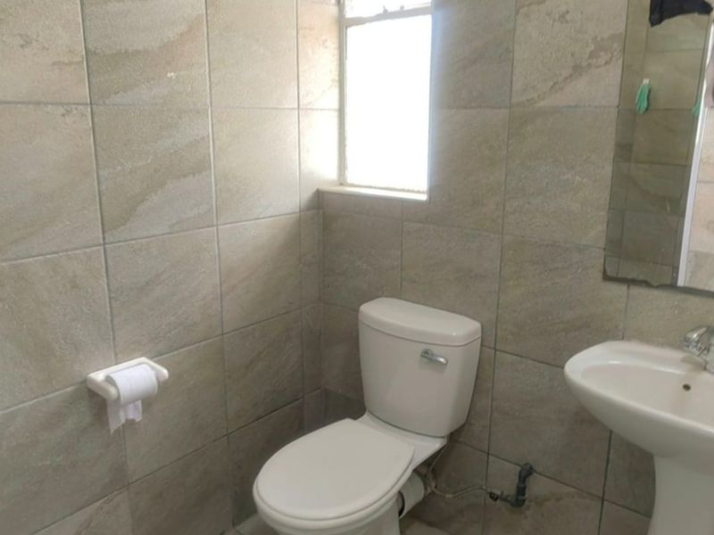 A functional bathroom featuring tiled walls and flooring, equipped with a standard pedestal basin and toilet.
