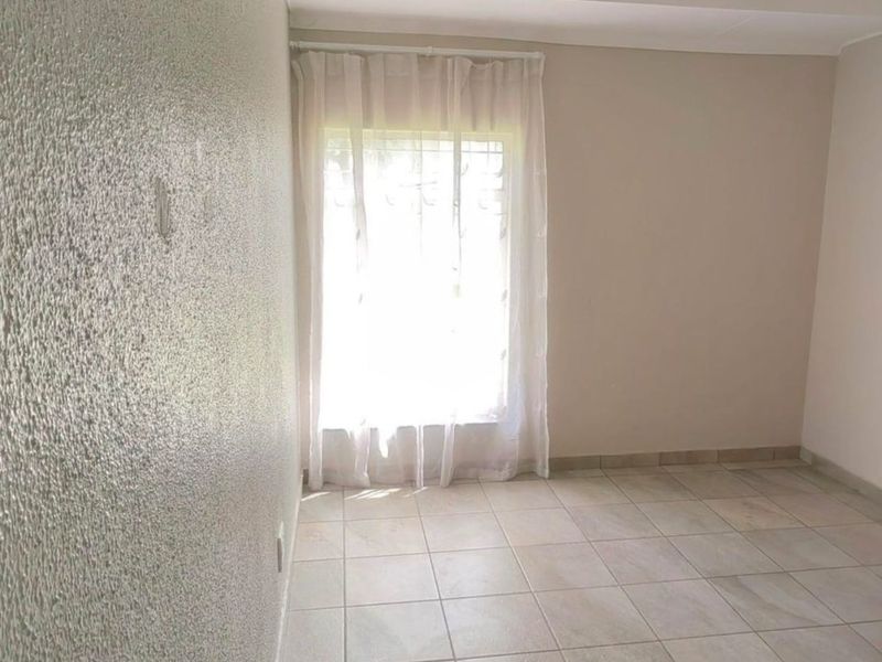 A vacant bedroom featuring neutral tiled flooring, textured walls, and a window fitted with security bars.