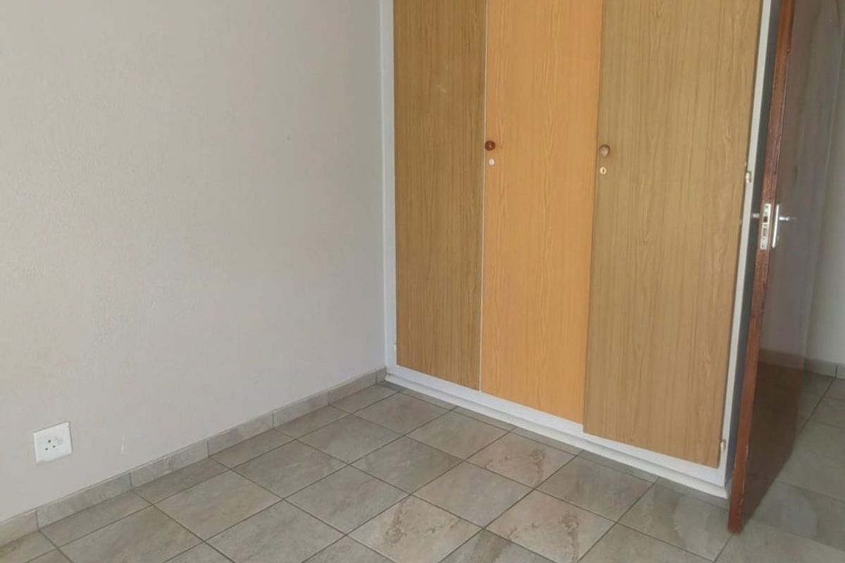 An empty bedroom featuring neutral tiled flooring and built-in wooden cupboards, providing a clean and functional space ready for personalization.