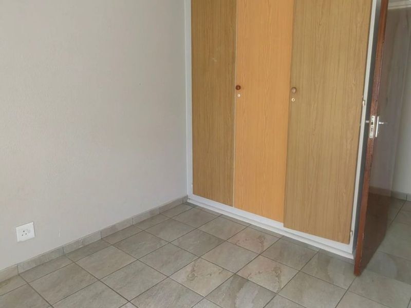 An empty bedroom featuring neutral tiled flooring and built-in wooden cupboards, providing a clean and functional space ready for personalization.
