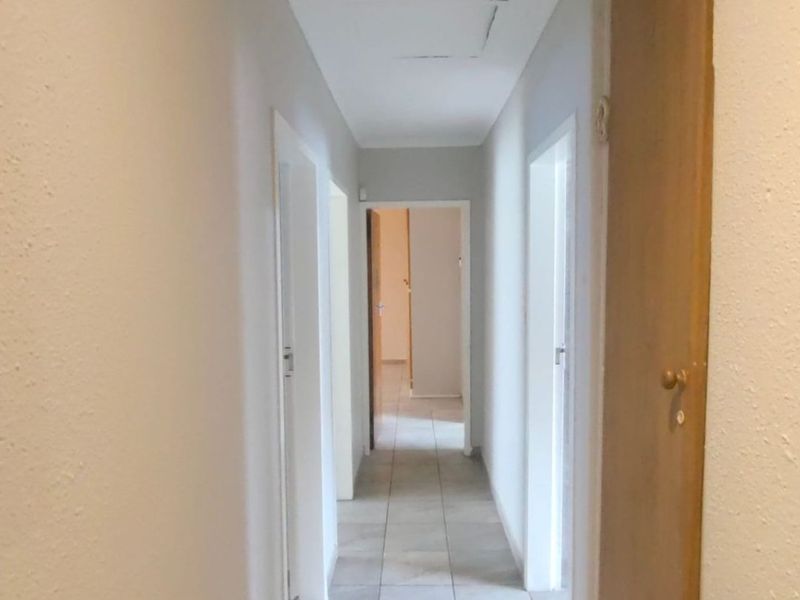 A functional, tiled hallway providing access to multiple rooms, featuring a neutral color palette and a ceiling access hatch.