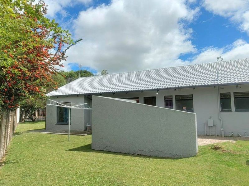 Rear view of the property featuring a tiled roof, a private garden with lawn, and a paved patio area with a concrete privacy wall.
