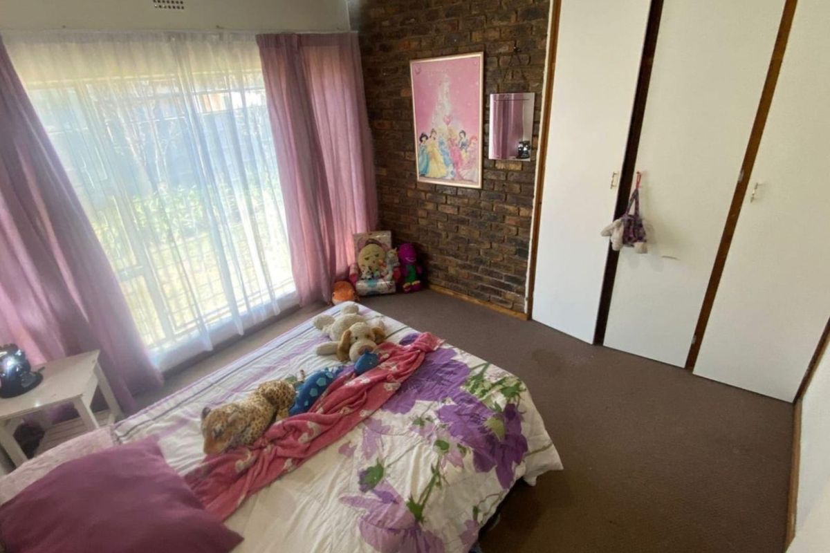 A bedroom featuring an exposed brick wall, built-in cupboards, and carpeted flooring, offering a functional space with potential for modern updates.