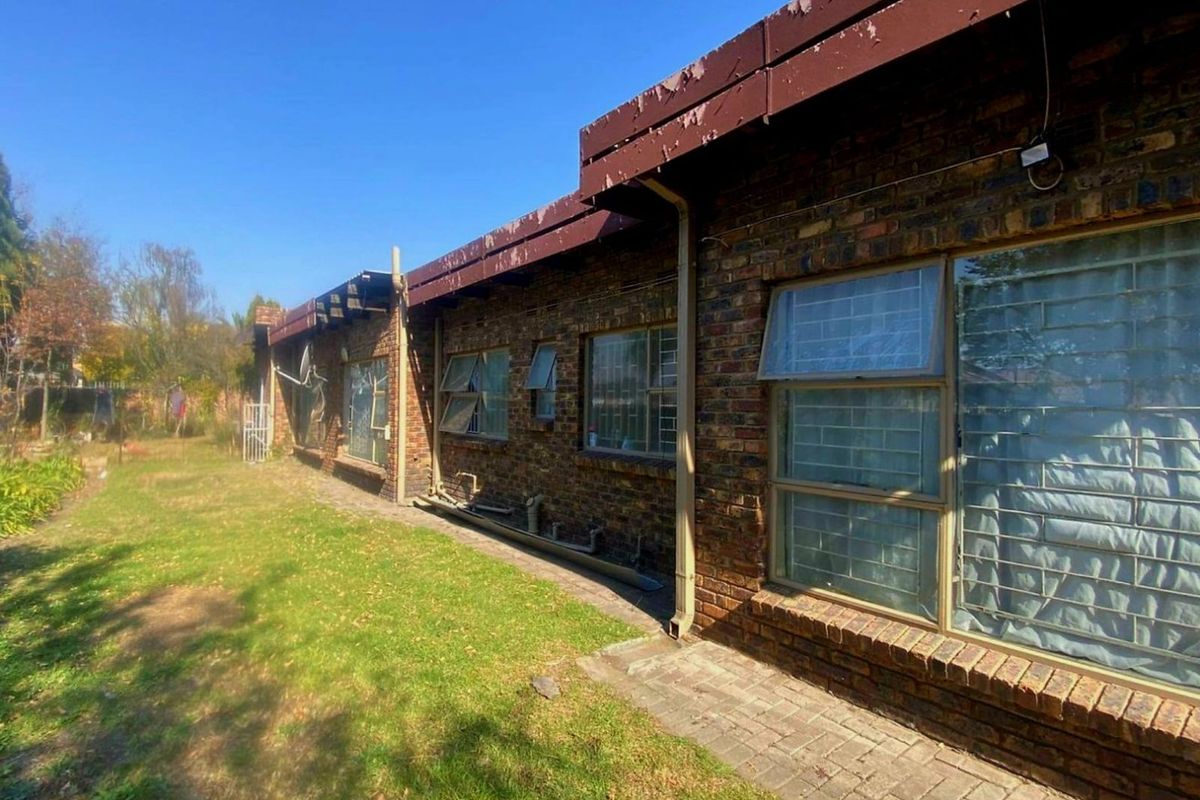 Rear exterior view of a face brick house featuring metal window frames with security bars and a paved walkway along the building perimeter.