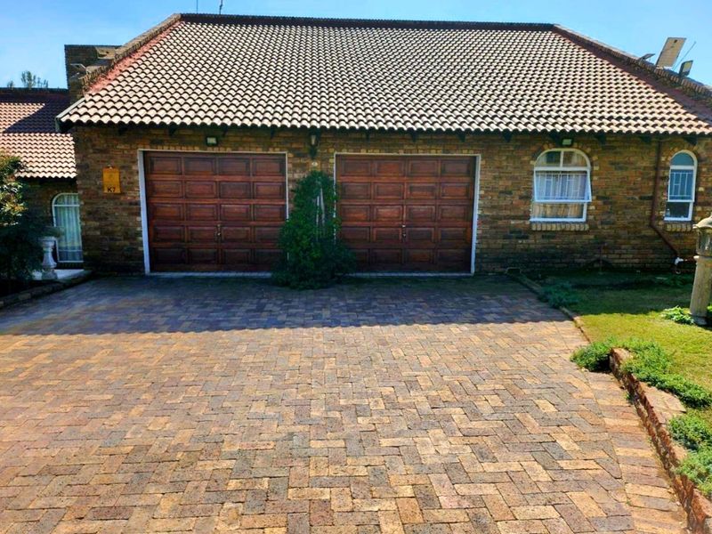 A well-maintained brick facade featuring a double garage with wooden doors, a paved driveway, and a tiled roof.