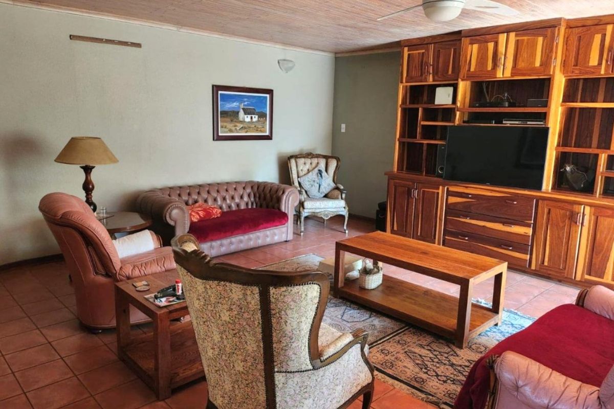 A spacious living room featuring terracotta floor tiles, a timber-clad ceiling, a ceiling fan, and a large built-in wooden wall unit.