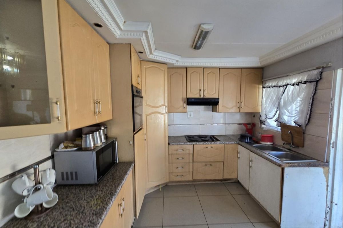 A functional kitchen featuring light wood cabinetry, granite countertops, built-in oven, hob, and extractor fan, with tiled flooring and coved ceiling details.