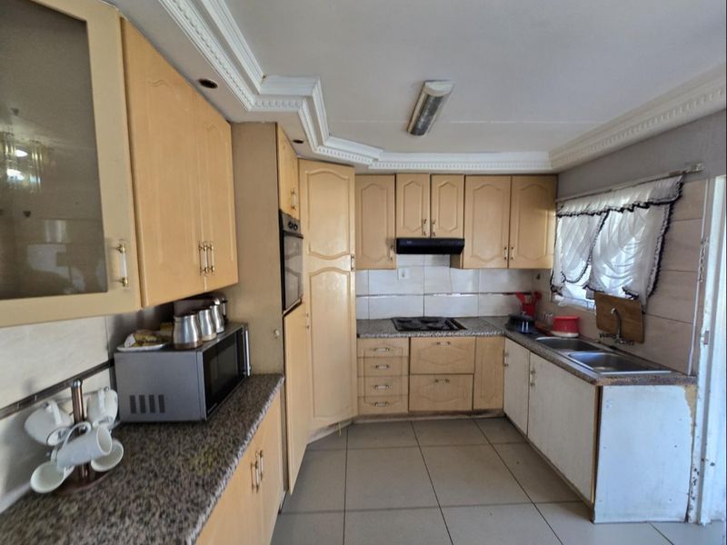 A functional kitchen featuring light wood cabinetry, granite countertops, built-in oven, hob, and extractor fan, with tiled flooring and coved ceiling details.