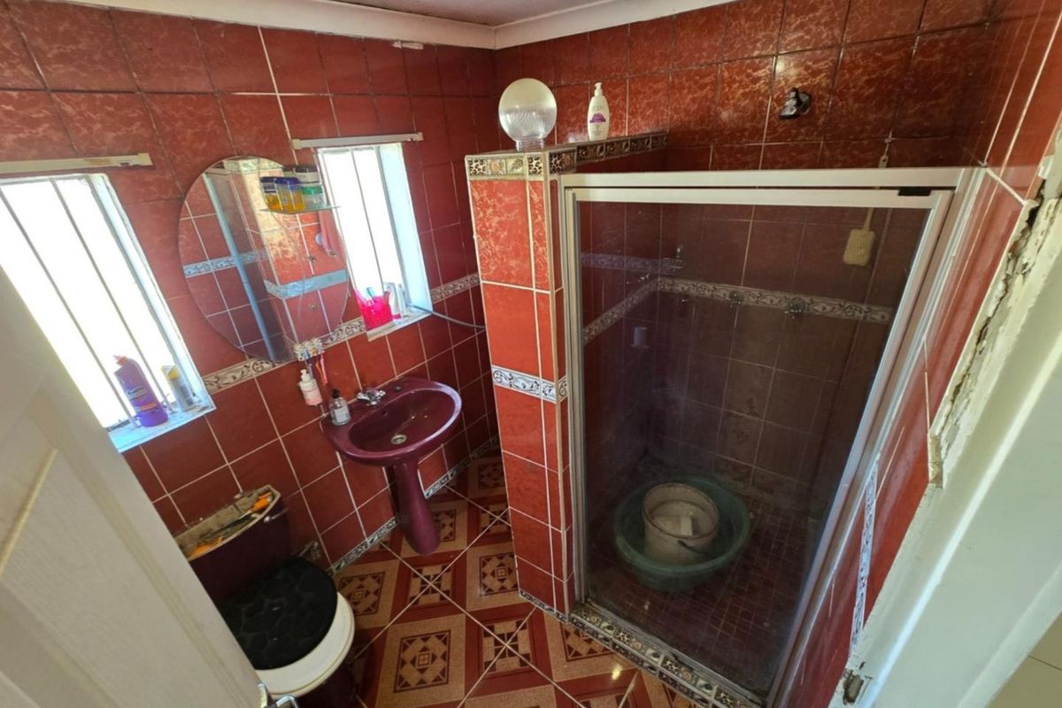A dated bathroom featuring red tiled walls and flooring, a pedestal sink, and a glass-enclosed shower, requiring significant cosmetic updates and repairs.