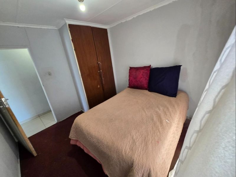 A compact bedroom featuring a built-in wooden wardrobe, coved ceiling, and carpeted flooring, offering a functional space with potential for cosmetic updates.