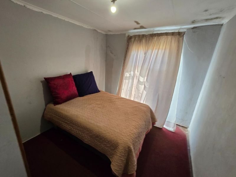 A bedroom featuring carpet flooring and a curtain rail, currently showing signs of significant wear including ceiling water damage and wall paint deterioration.