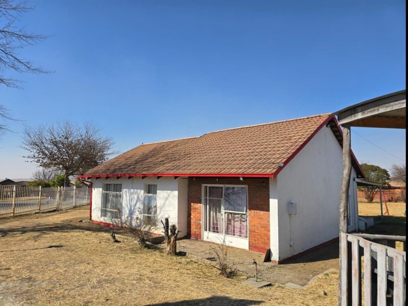 Rear view of a single-story detached house featuring a tiled roof, brick and plaster facade, and a sliding glass door leading to the garden.