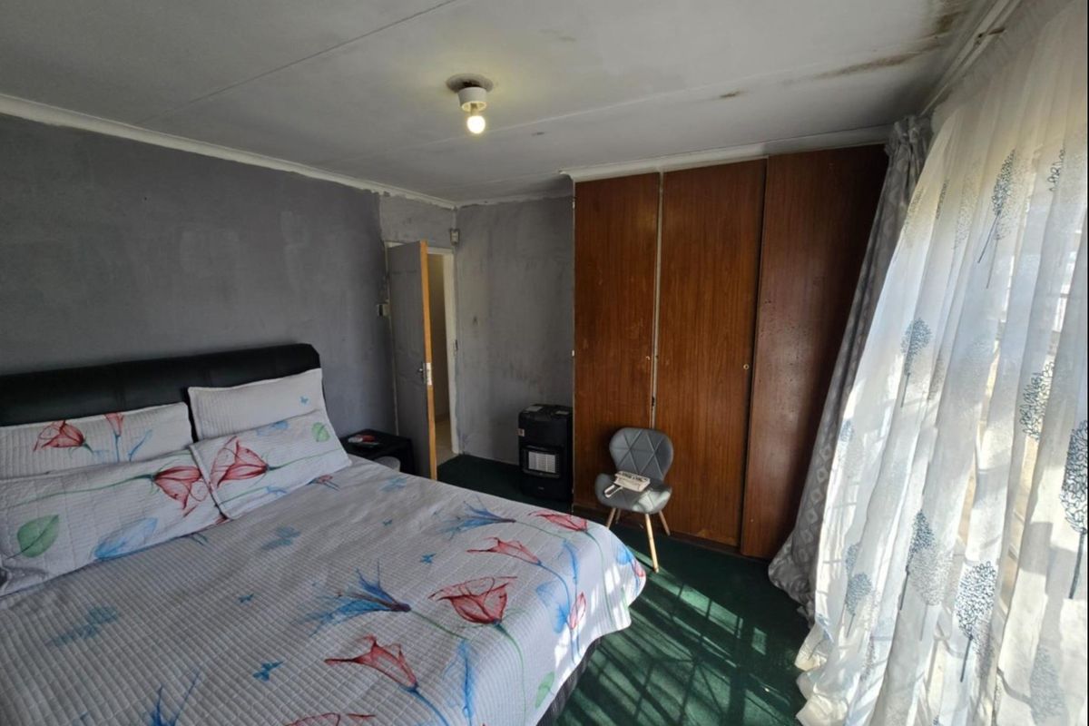 A bedroom featuring built-in wooden wardrobes and carpeted flooring, currently showing signs of ceiling water damage and dated wall finishes.