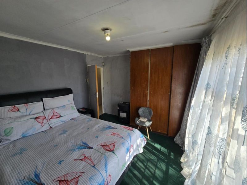 A bedroom featuring built-in wooden wardrobes and carpeted flooring, currently showing signs of ceiling water damage and dated wall finishes.