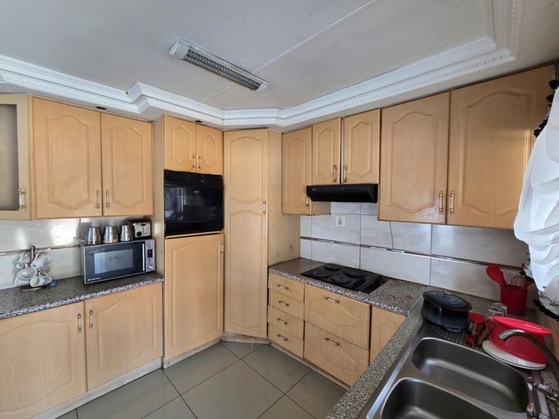 A functional kitchen featuring light wood cabinetry, granite countertops, built-in oven, electric hob, and a double stainless steel sink with tiled flooring.