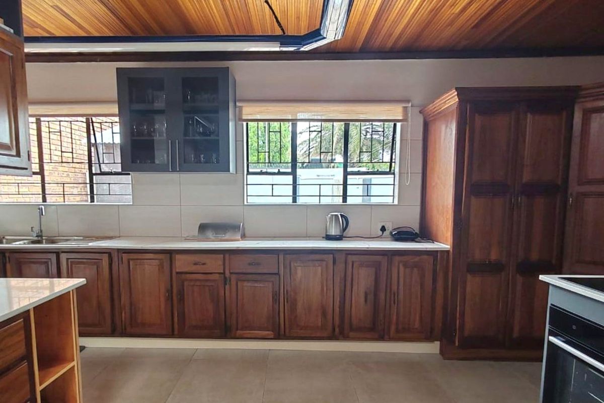 A kitchen featuring wooden cabinetry, tiled countertops, and a distinctive timber-paneled ceiling, offering a traditional aesthetic with functional storage space.