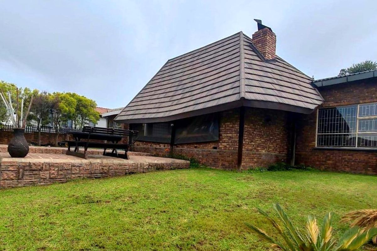 Rear view of the property featuring a brick facade, a pitched tiled roof with a chimney, and an elevated paved patio area overlooking the garden.