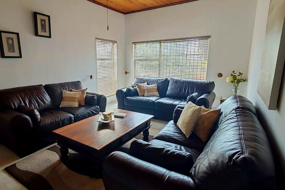 A comfortable living room featuring a high timber-paneled ceiling, neutral walls, and large windows fitted with horizontal blinds.