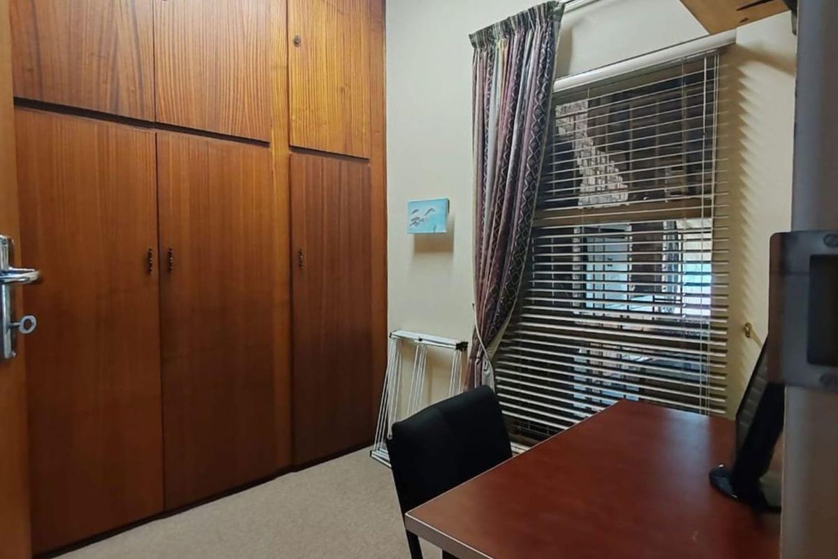 A functional bedroom featuring floor-to-ceiling built-in wooden cupboards and a window with fitted blinds.