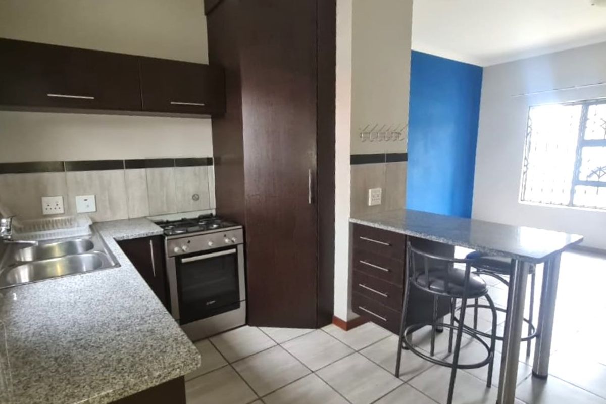 A functional kitchen featuring dark wood cabinetry, granite countertops, a gas stove, and an integrated breakfast bar with tiled flooring.