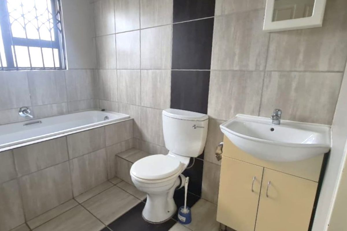A functional bathroom featuring a built-in bathtub, vanity cabinet with basin, and neutral wall and floor tiling with a decorative dark accent strip.
