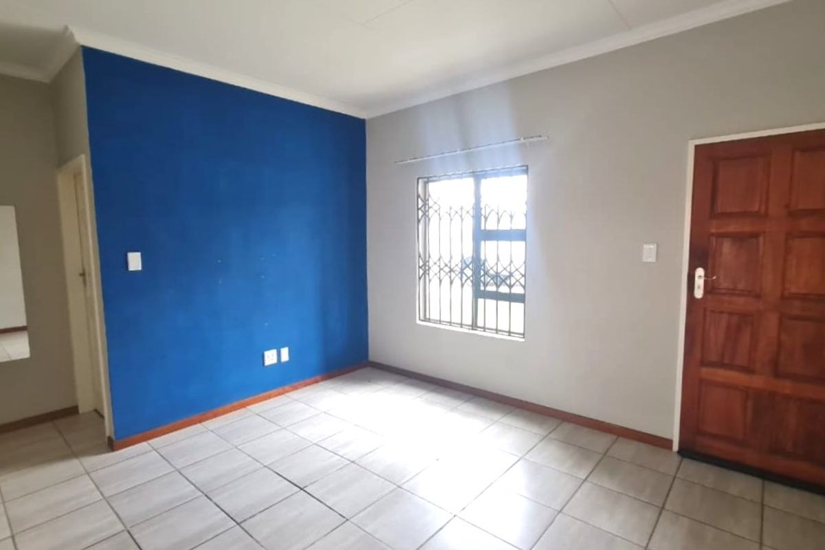 An empty bedroom featuring tiled flooring, a security gate on the window, and a wooden door, ready for personalization.