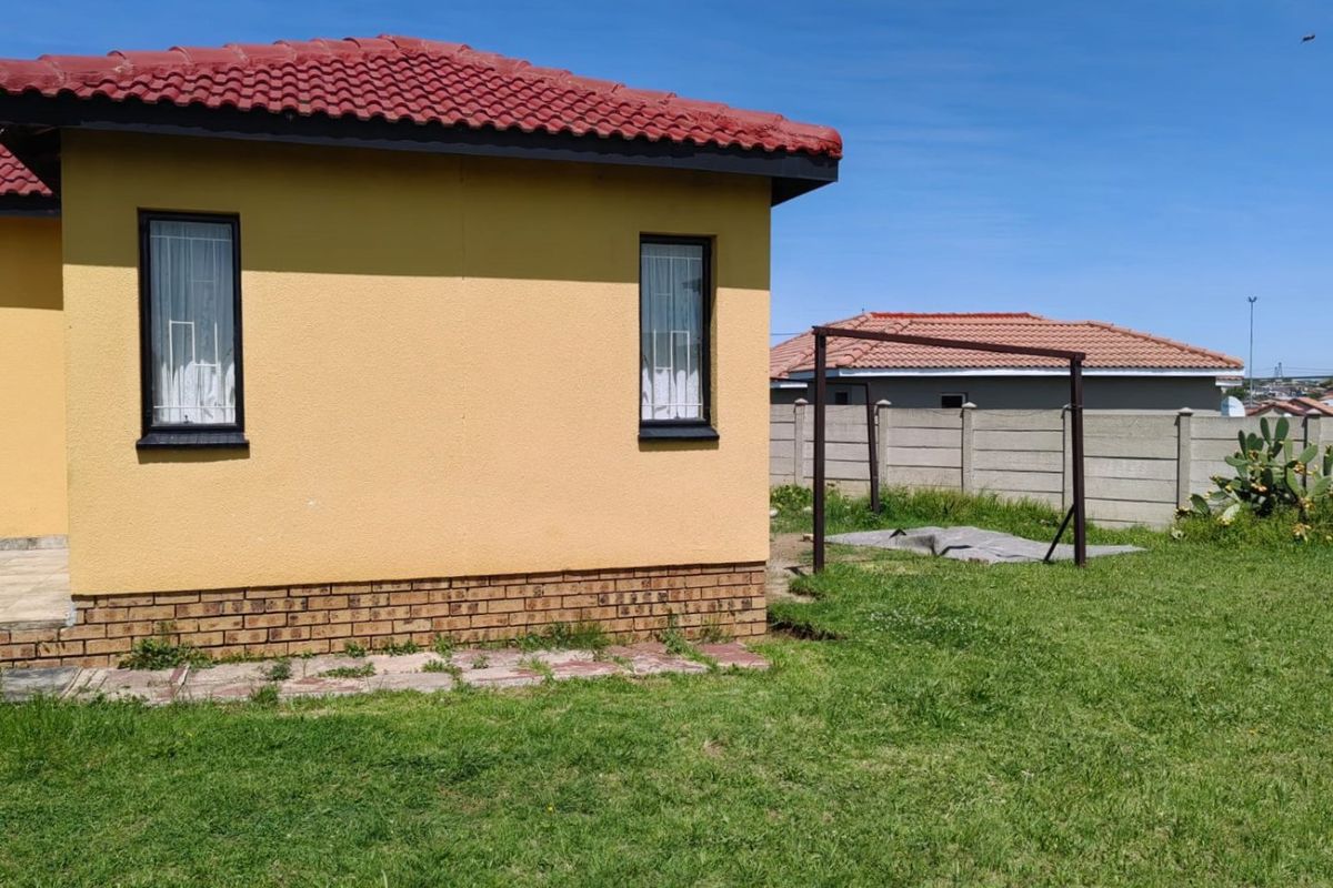 Rear view of the property featuring a yellow facade, tiled roof, and a private garden enclosed by a precast concrete boundary wall.