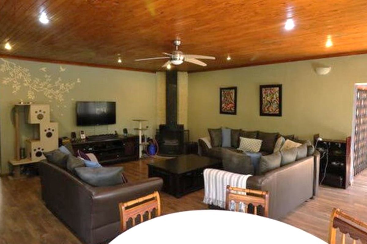 Spacious living room featuring a wood-burning fireplace, timber-clad ceiling, and ceiling fan, creating a warm and inviting atmosphere.